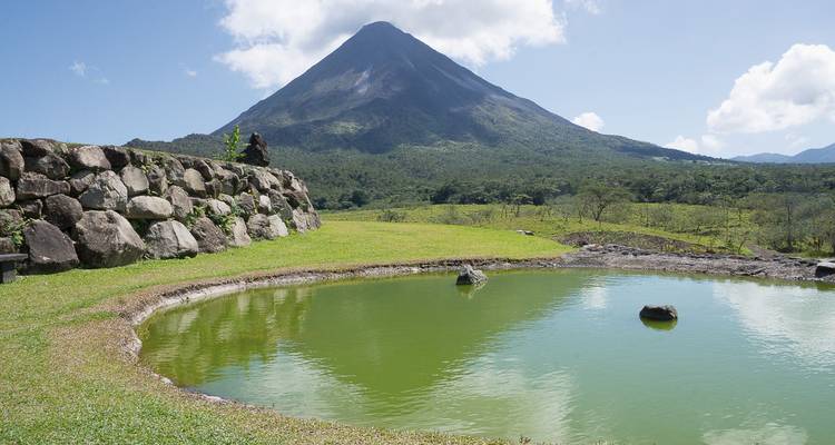 Arenal Volcano with a clear sky and a small pond in the foreground.