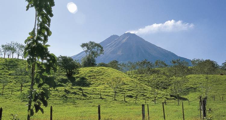 Scenic view of Arenal Volcano with green pastures in the foreground.