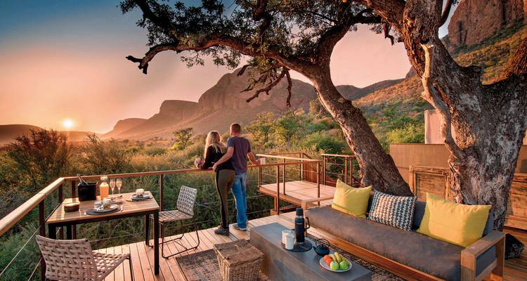 Un couple savourant un verre sur une terrasse avec une vue imprenable sur les montagnes au coucher du soleil.