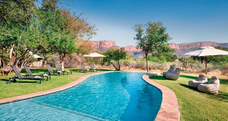 Une piscine dans un jardin ensoleillé avec vue sur les montagnes.