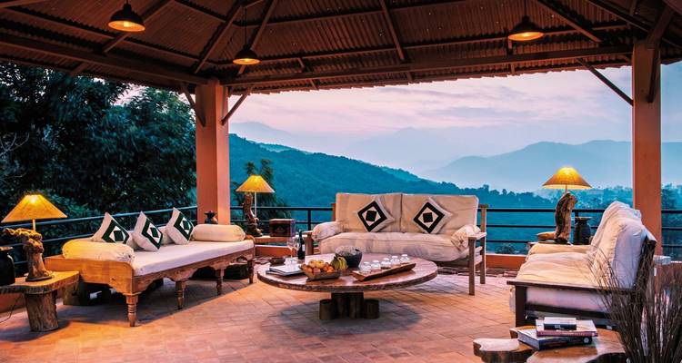 Eine überdachte Terrasse mit bequemen Sitzgelegenheiten und Bergblick bei Sonnenuntergang.