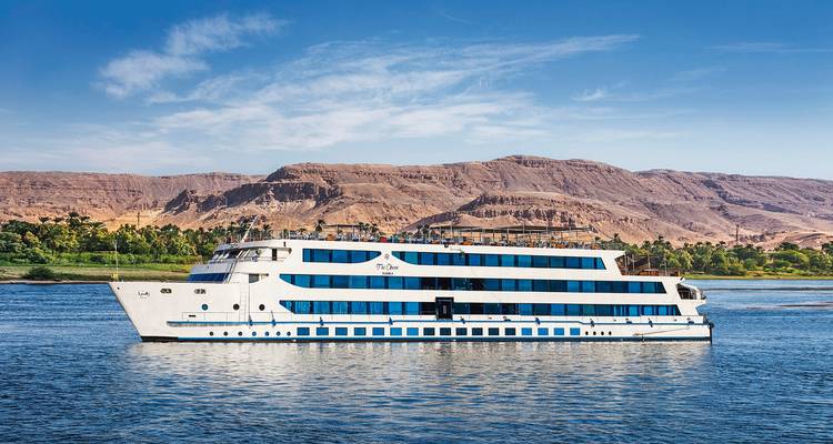 Crucero blanco navegando por un río con paisaje desértico.