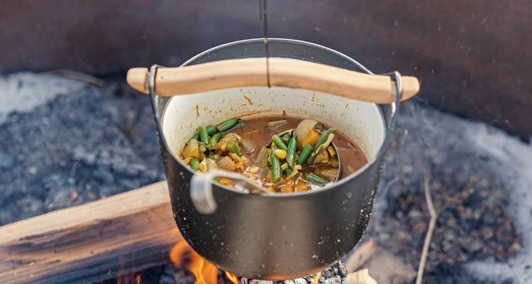 A pot of soup cooking on a campfire.