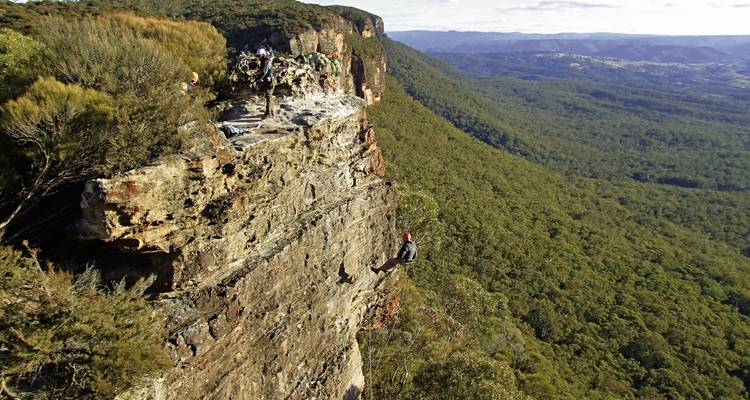 Escalador descendiendo en rappel por una pared rocosa con un valle boscoso abajo.
