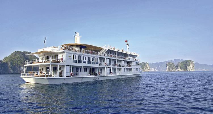 Navire de croisière en mer par temps clair avec des formations calcaires en arrière-plan.