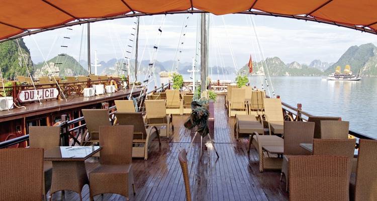 Pont d'un navire de croisière avec des sièges vides donnant sur la baie d'Halong.