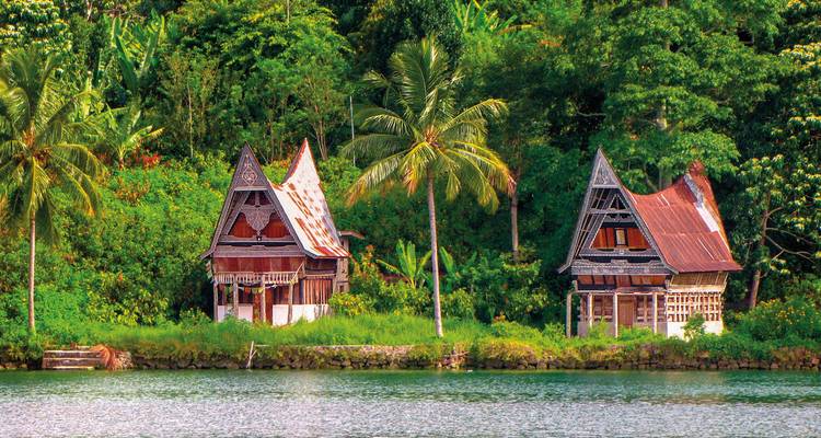 Traditional Indonesian houses by a river with lush greenery.