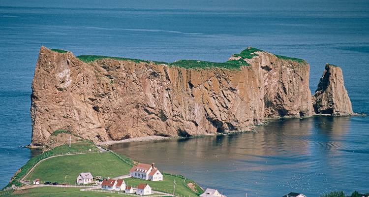 Une grande formation rocheuse au bord de la mer avec de petits bâtiments et une croix.