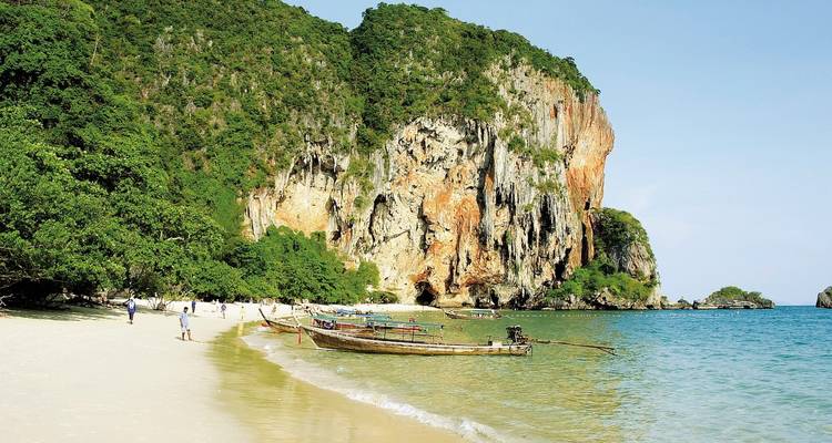 Plage tropicale avec bateaux à longue queue, sable blanc et falaises calcaires imposantes