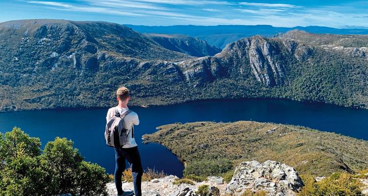 Hiker overlooking a lake and mountains from a high viewpoint.