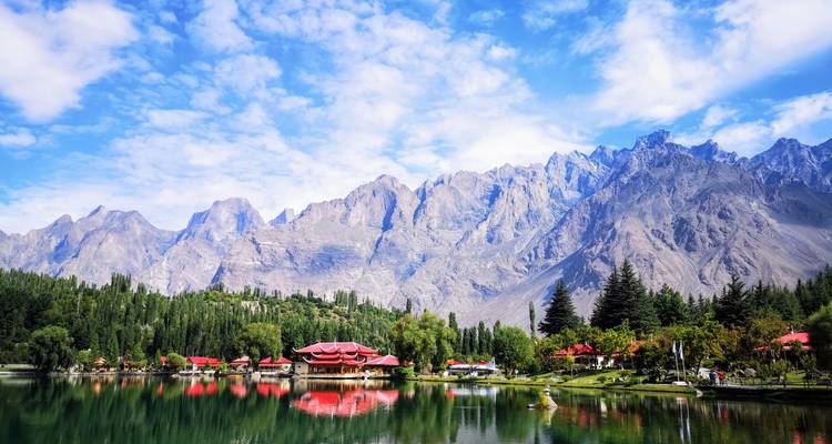 Mirror-calm lake reflecting red pavilions and stark granite peaks under a blue sky.