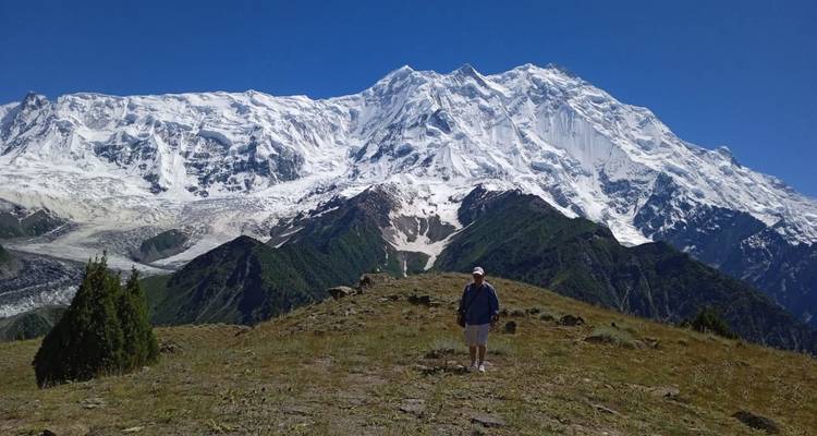 A traveler standing on alpine grassland before the immense snow-covered face of Nanga Parbat.