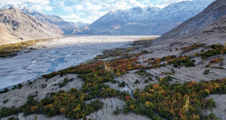 Drone view of a river delta with colorful autumn foliage framed by barren mountains.