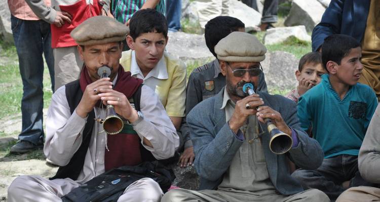 Local musicians playing traditional horns while onlookers listen during an outdoor gathering.