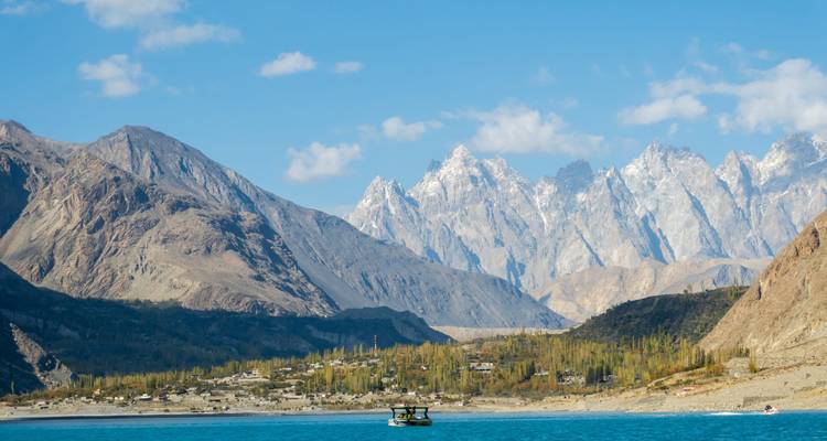 Turquoise lake with a small boat set against jagged peaks under a bright sky.