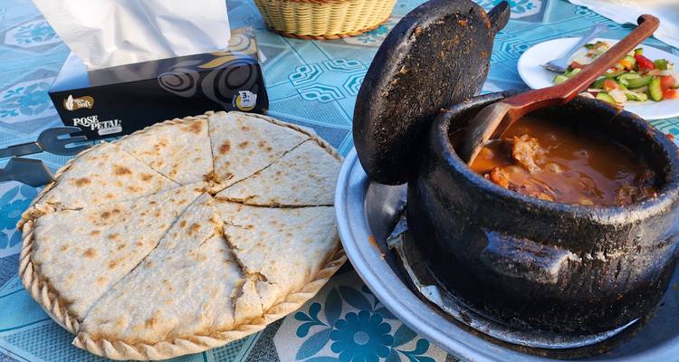 Traditional Pakistani meal with a hot stew in a black pot and a large flatbread on a patterned table.