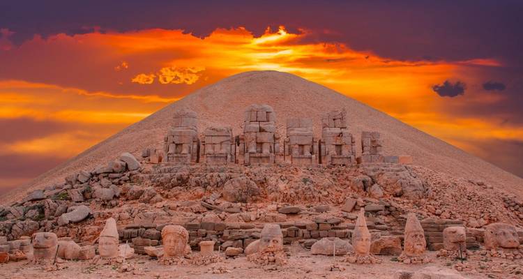 Ancient stone heads at the summit of a mountain with a sunset backdrop.