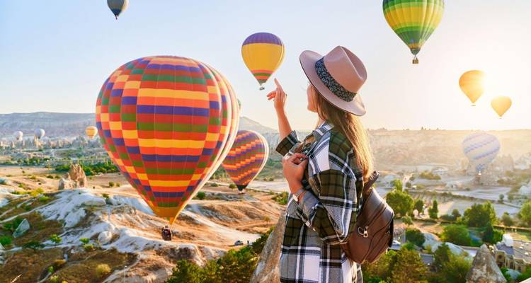 Person interacting with colorful hot air balloons over Cappadocia.