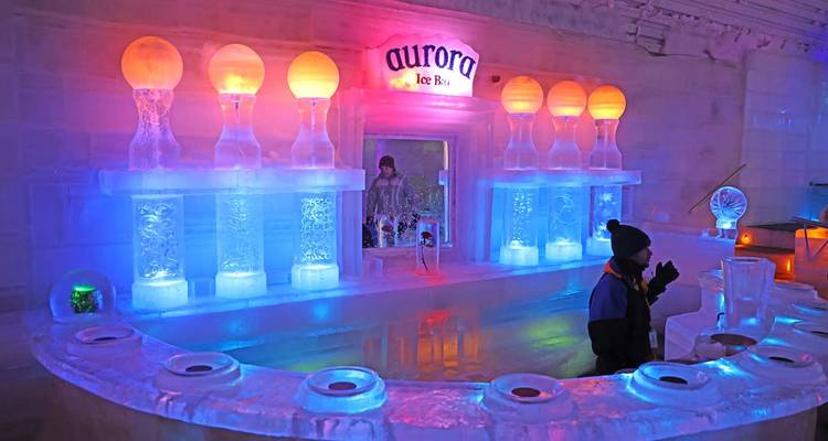 Intérieur d'un bar de glace illuminé par des couleurs à Fairbanks avec comptoir en glace sculpté, sphères lumineuses et clients vêtus de vêtements d'hiver.