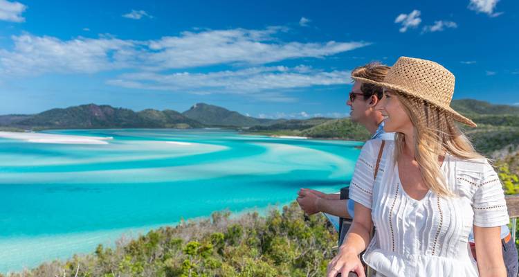 Una pareja admira los deslumbrantes remolinos turquesas de Whitehaven Beach desde un mirador en la cima de una colina.