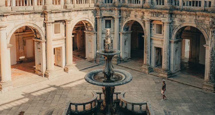 Weathered cloister courtyard in Tomar with central fountain and renaissance arches bathed in warm light.