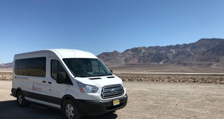 Furgoneta blanca estacionada en una carretera del desierto con montañas áridas al fondo.