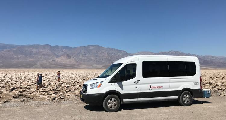 Furgoneta blanca estacionada en una zona desértica rocosa con montañas al fondo.