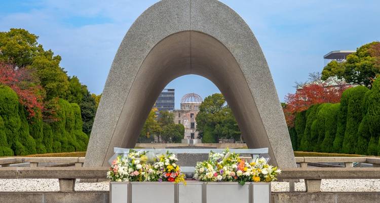 Cénotaphe du Mémorial de la Paix d'Hiroshima encadrant le Dôme de la Bombe Atomique avec des hommages floraux
