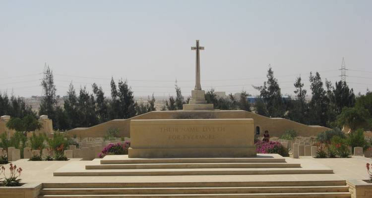 Monument de pierre et croix au cimetière de guerre d'El Alamein sous un ciel désertique brumeux.