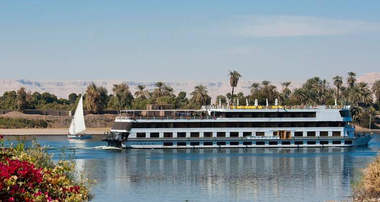 Bateau de croisière moderne sur le Nil et une felouque traditionnelle naviguant sur le fleuve calme bordé de palmiers.