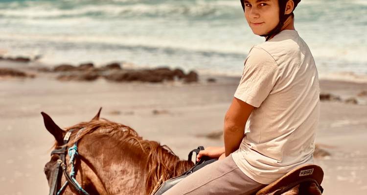 Junge zu Pferd am Meer blickt zurück.