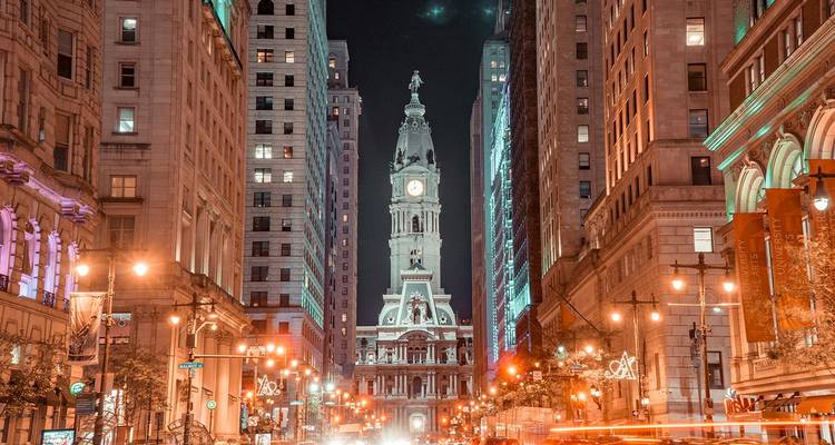 Paisaje nocturno de la calle Broad de Filadelfia que conduce al Ayuntamiento iluminado, con rastros de luces de autos.