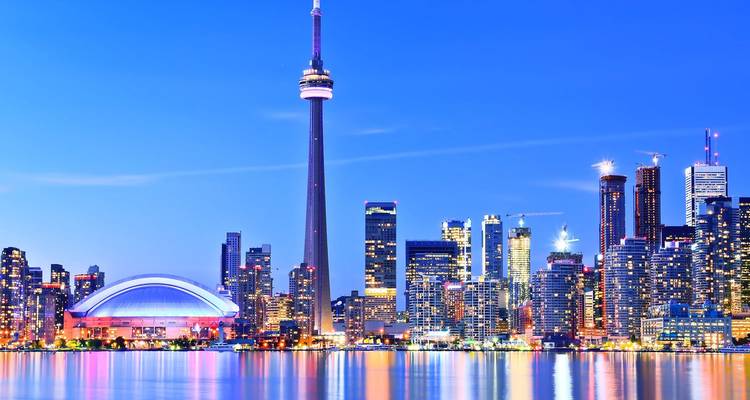 El resplandeciente horizonte nocturno de Toronto reflejado en el lago Ontario con la Torre CN dominando la escena.