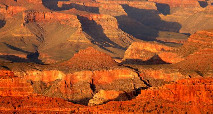 Les formations de roches rouges en couches et les vallées profondes du Grand Canyon baignent dans une lumière chaleureuse.