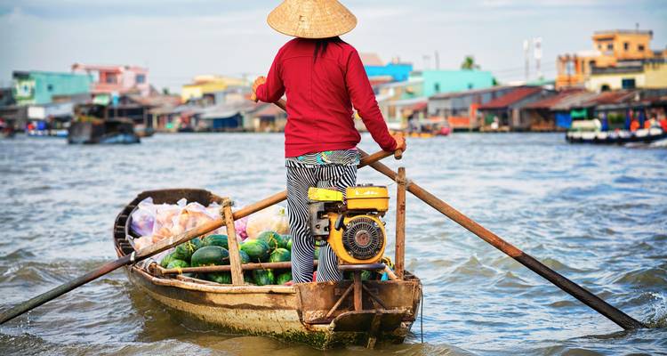 Person rowing a boat filled with watermelons on a river.