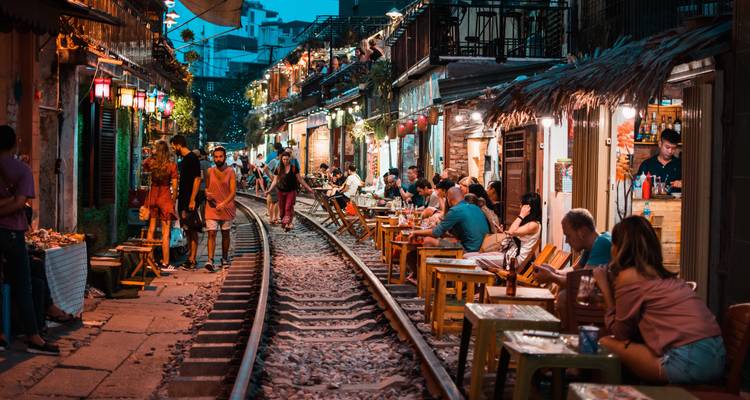 A bustling train street in Hanoi with people dining beside the tracks.