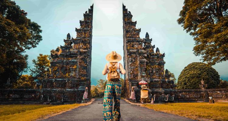Una persona parada frente a puertas tradicionales balinesas, usando un sombrero y una mochila.