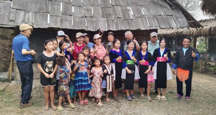 Eine große Gruppe von Dorfbewohnern und Reisenden posiert zusammen vor einem rustikalen Holzhaus im ländlichen Laos.