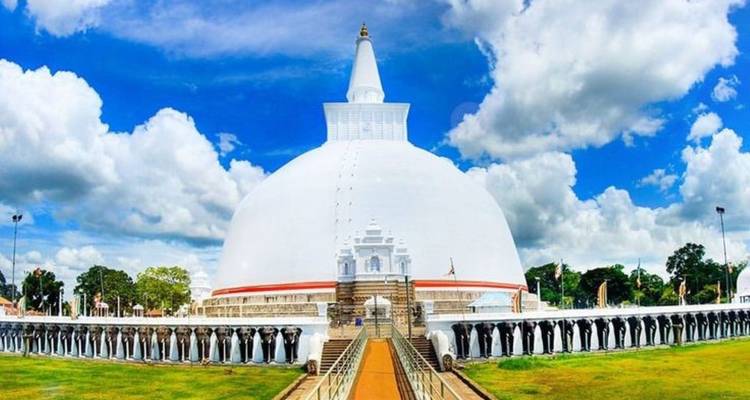 Strahlend weiße Ruwanwelisaya-Stupa unter dramatischen Wolken, umgeben von einer Elefantenfries-Mauer.