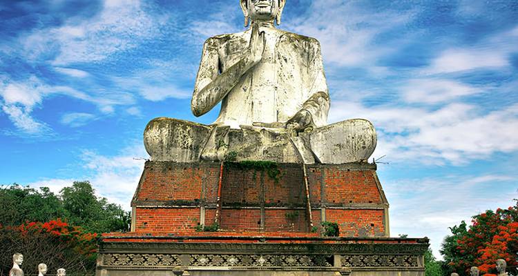 Large white Buddha statue seated atop a brick pedestal beneath a bright sky.