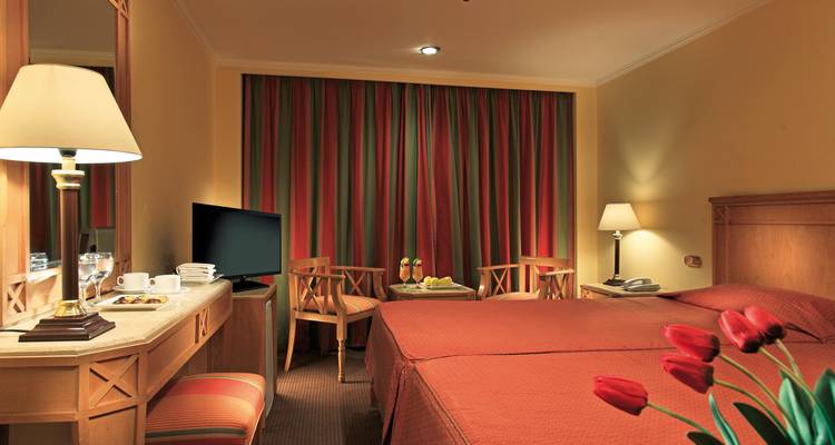 Ein Hotelzimmer mit einem Doppelbett und Stühlen neben einem Fenster mit geschlossenen Vorhängen.