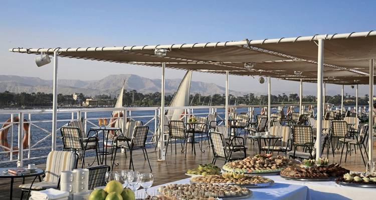 Restaurants im Freien mit gedeckten Tischen auf einer Terrasse mit Blick auf den Nil und die umliegenden Berge.