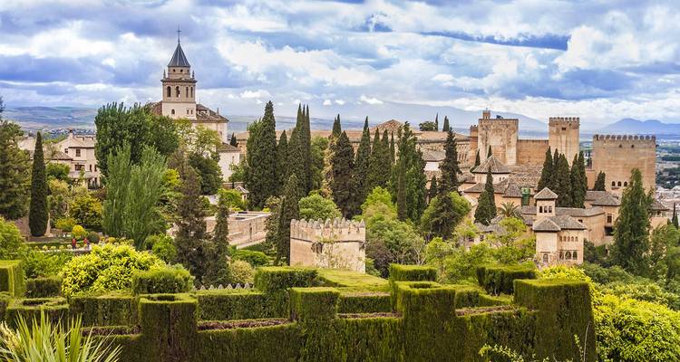 Palacio histórico y exuberantes jardines rodeados de cipreses y murallas de piedra con vistas a la ciudad.