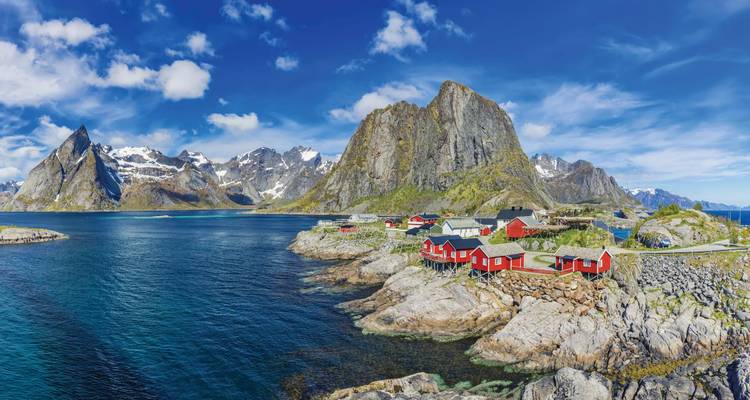 Scenic view of a fjord with red cabins and towering mountains.