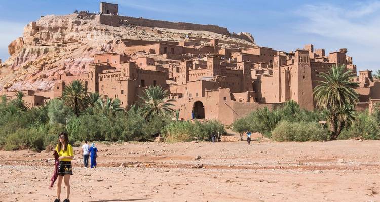 Historische Stätte mit einem befestigten Dorf und Palmen, mit Touristen im Vordergrund.