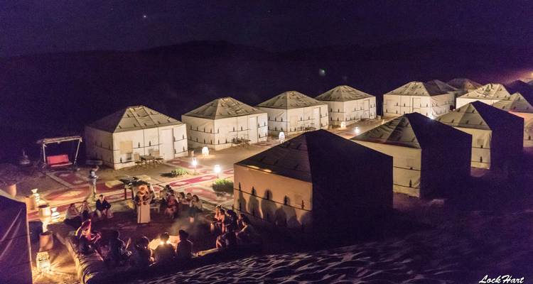 Nächtlicher Campingplatz mit Zelten und einer kleinen Versammlung um ein Feuer.