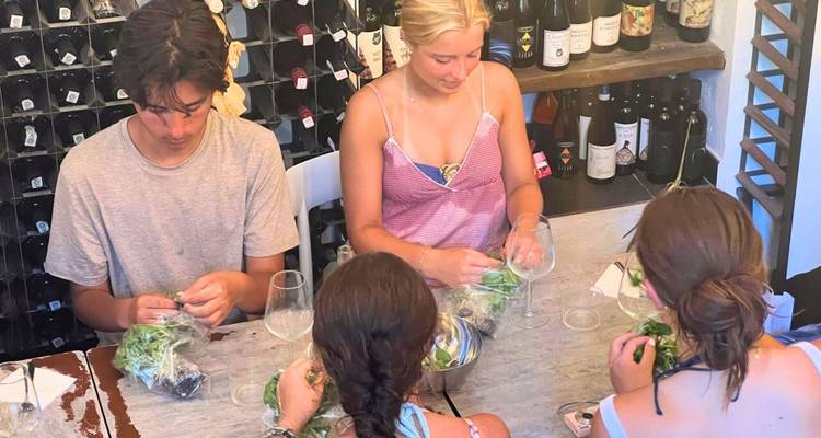 Des personnes assises à une table préparant de la nourriture avec des bouteilles de vin en arrière-plan.