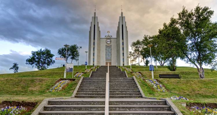 Iglesia de Akureyri con escalones que conducen hacia ella, rodeada de flores y árboles.