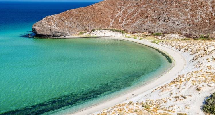 Een schilderachtig strand met helder turquoise water en een kleine rotsachtige heuvel.