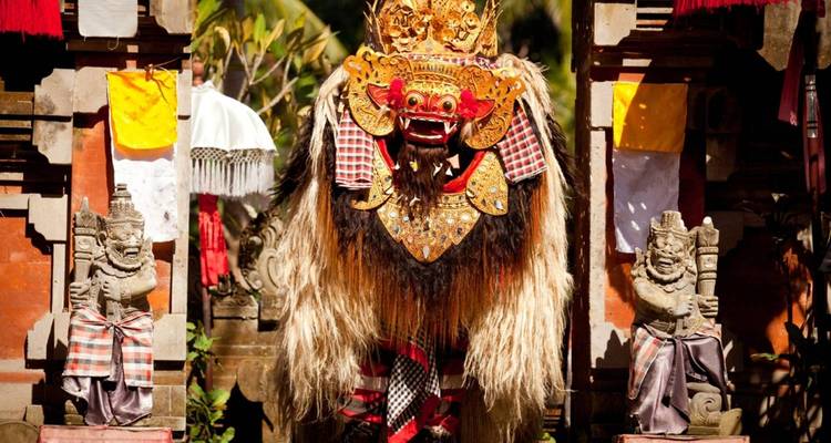 Costume traditionnel de danse Barong balinaise encadré par des statues de portail de temple.